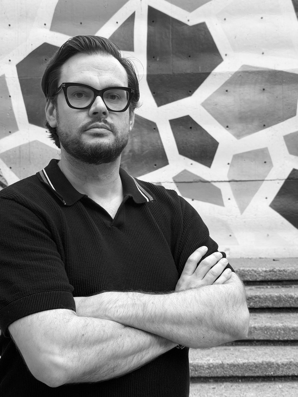 Taylor Dwyer, founder of Backwerd Rhythm Shop — a black-and-white portrait, arms crossed, in front of a painted concrete wall.